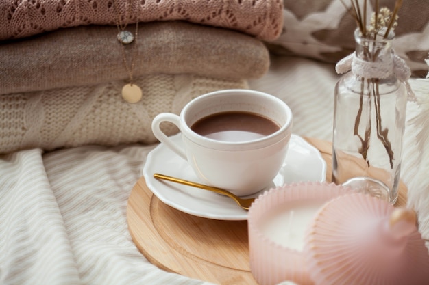 Eine Tasse heißen Kakao, gestrickte Pullover, ein Strauß weißer Trockenblumen in einer Vase, eine Kerze auf dem Bett. Frühstück im Bett. Gemütlich. Frühling.