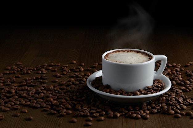 Eine Tasse heißer Cappuccino auf einer Untertasse und gestreuten Kaffeebohnen