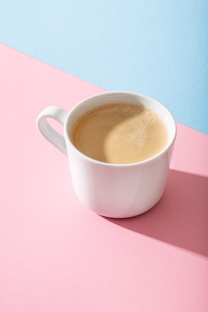 Eine Tasse Kaffee auf einem pastellrosa und blauen Hintergrund,