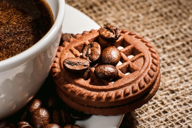 Eine Tasse Kaffee auf Sackleinen und KeksenEine Tasse frisch zubereiteter Kaffee raucht Zimtstangen