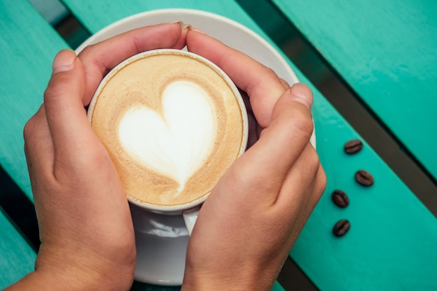 Eine Tasse Kaffee-Cappuccino mit Herz auf einem grünen Tisch. Konzept eines romantischen Morgens und Frühstücks