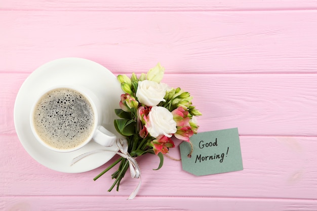 Eine Tasse Kaffee, ein Blumenstrauß und eine Karte mit den Worten Guten Morgen