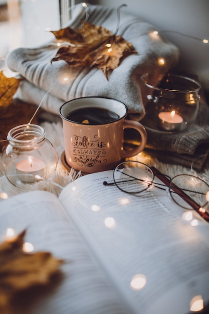 Eine Tasse Kaffee, ein Buch auf einer weißen Decke, Kerzen, Gläser.