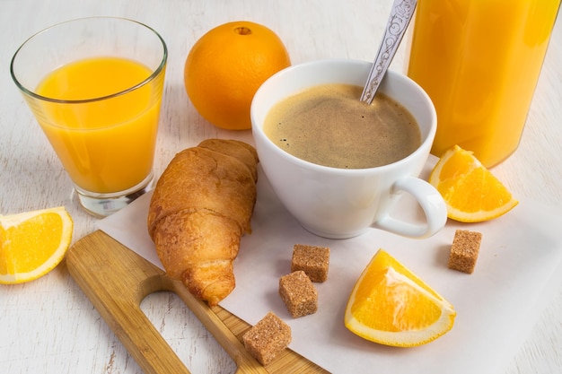 Eine Tasse Kaffee, frische Orangen, Orangensaft und Croissant auf weißem Hintergrund Frühstück-Konzept