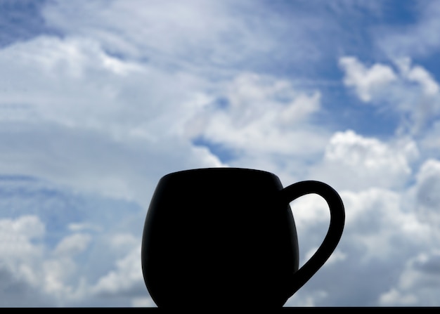 Eine Tasse Kaffee im Gegenlicht mit Wolken im Hintergrund des blauen Himmels