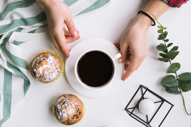 Eine Tasse Kaffee in den Händen und Muffins auf einer weißen Oberfläche und Muffins