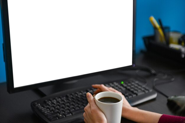 Eine Tasse Kaffee in der Hand am Computer