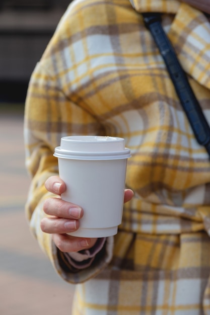 Eine Tasse Kaffee in einer Einweg-Tasse in den Händen einer stilvollen Frau im Stadtbecher-Entwurfsmodell