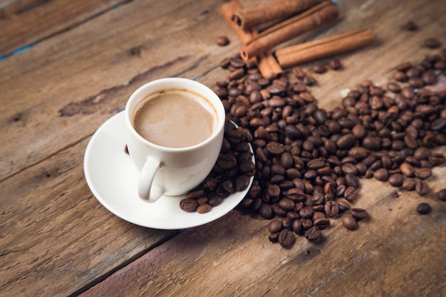 Eine Tasse Kaffee, Kaffeesamen, Zimt und ein Buch auf einem Holztisch