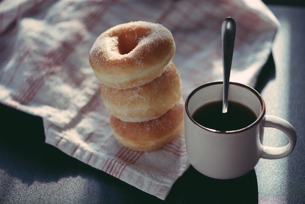 Eine Tasse Kaffee mit einem Löffel neben einem Stapel Donuts.