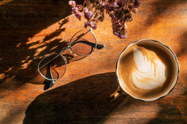 Eine Tasse Kaffee mit Latte Art und Gläsern auf Holztisch im Café, Draufsicht.