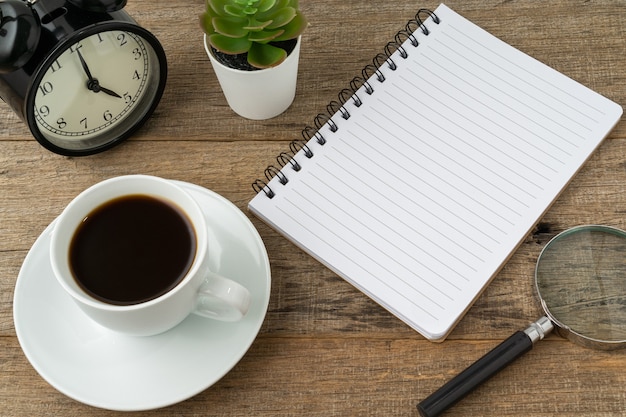 Eine Tasse Kaffee und ein Notizbuch mit einem Kopierraum auf Holzbrett.