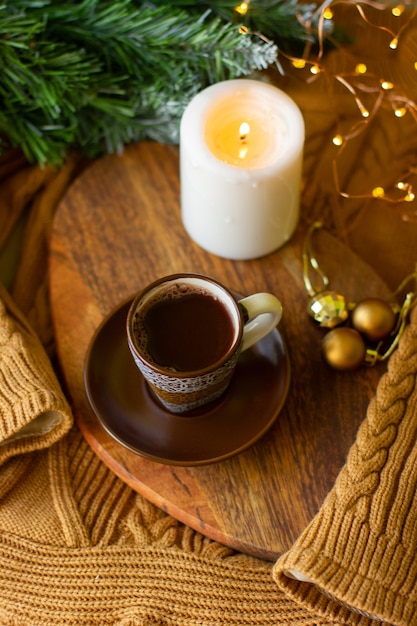 eine Tasse Kaffee und eine Kerze an einer Tafel auf einem gemütlichen warmen Pullover und einem Zweig eines Weihnachtsbaumes