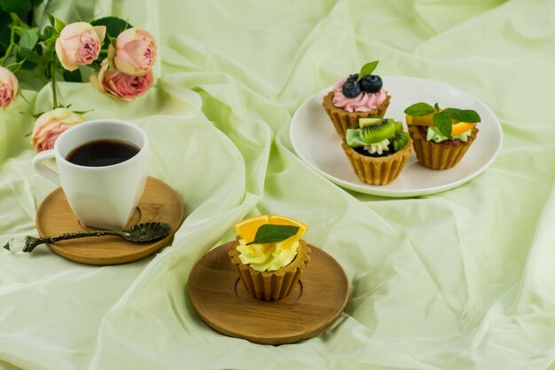 Eine Tasse Kaffee und Mini-Tortillas mit Sahne und frischem Obst auf einem Teller. zarter Pastellhintergrund mit einem Rosenstrauß.