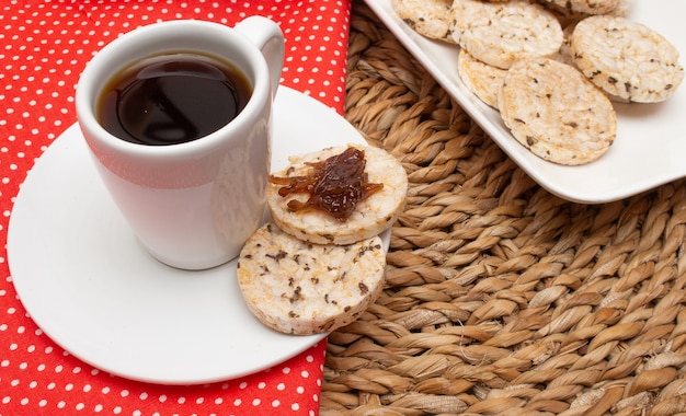 Eine Tasse Kaffee unter dem Strohtisch, umgeben von einer Schüssel voller Reiskekse und einer Kaffeekanne