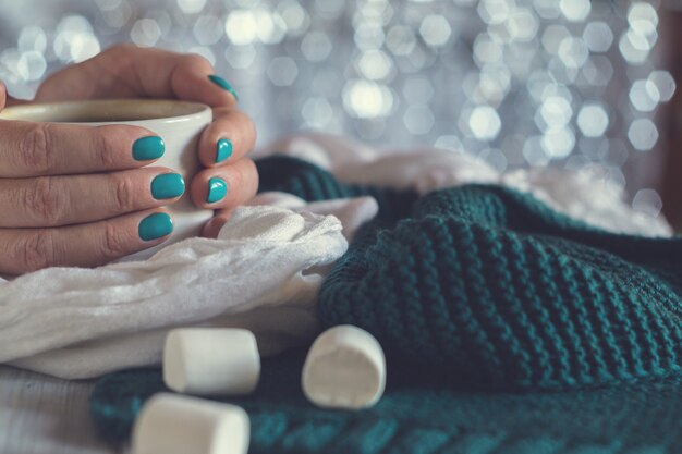 Eine Tasse Kakao mit Marshmallow in weiblichen Händen mit blauer Maniküre auf glänzendem Hintergrund