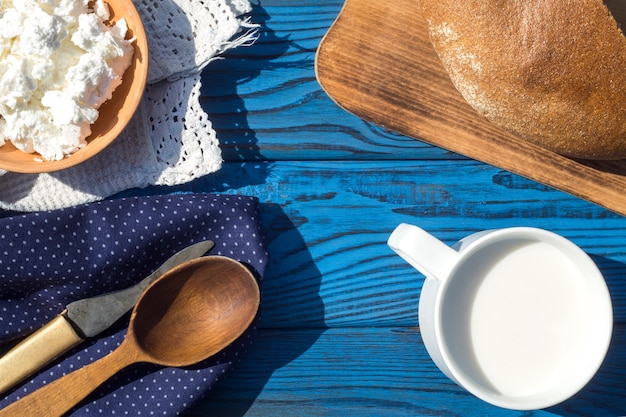 Eine Tasse Milch, Hüttenkäse und Brot auf einem Tisch aus blauen Brettern. Ansicht von oben