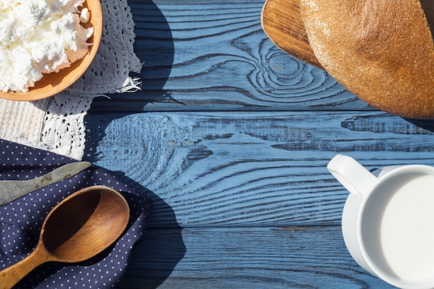 Eine Tasse Milch, Hüttenkäse und Brot auf einem Tisch aus blauen Brettern. Ansicht von oben