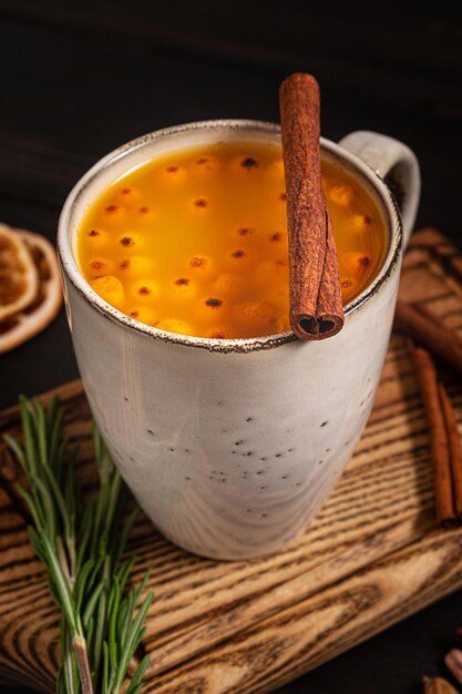 Eine Tasse Sanddorn-Heißgetränk, serviert mit Rosmarin und Zimt, auf dunklem Holzhintergrund