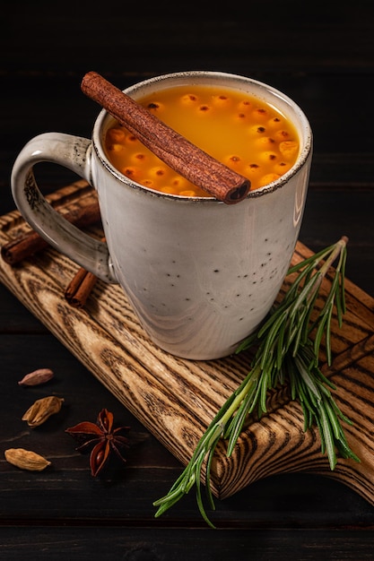 Foto eine tasse sanddorn-heißgetränk, serviert mit rosmarin und zimt, auf dunklem holzhintergrund