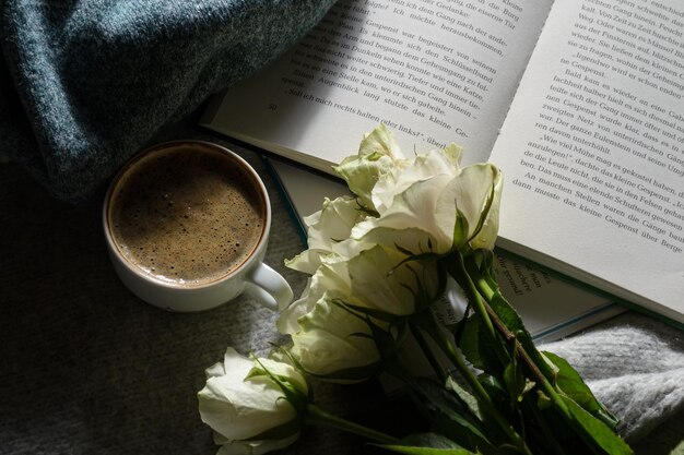 Eine Tasse schwarzen heißen Kaffee, ein interessantes Buch, ein Strauß weißer Rosen und ein warmer Pullover