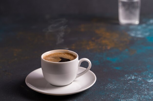 Eine Tasse schwarzen Kaffees in einer Tasse auf blauem Brett, unscharfer Hintergrund.