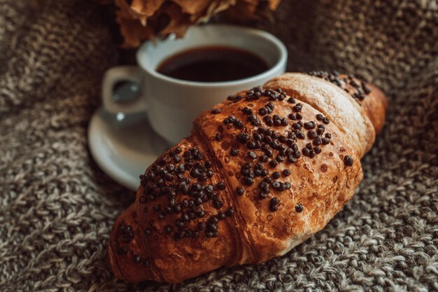 Eine Tasse schwarzen Morgenkaffee mit einem frischen Schokoladencroissant. Köstliche Mahlzeit. Ästhetik im Detail