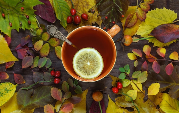 Eine Tasse Tee auf einem Hintergrund von mehrfarbigen Herbstblättern auf einer Holzoberfläche