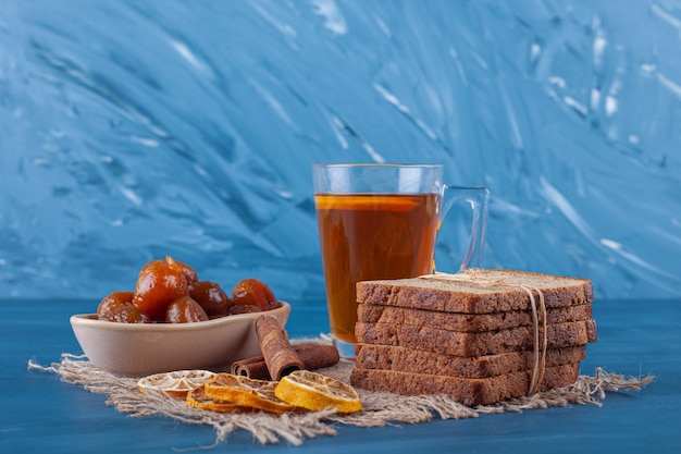 Eine Tasse Tee, geschnittenes Brot und Feigenmarmelade auf einem Handtuch, auf dem blauen Hintergrund.