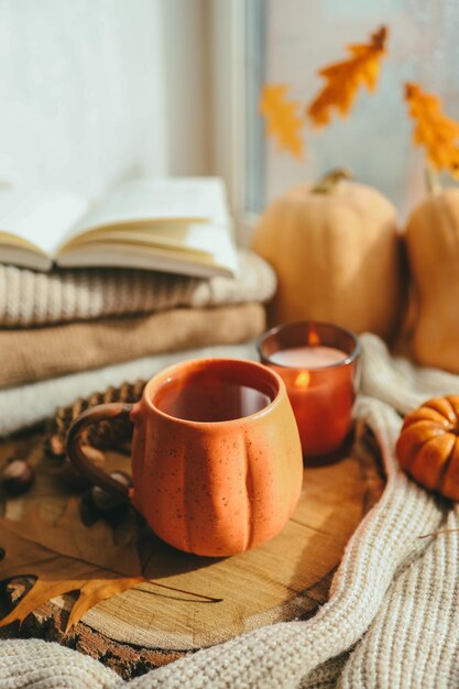 Eine Tasse Tee in Form eines Kürbises vor dem Hintergrund von Stapeln von Pullovern Herbststimmung