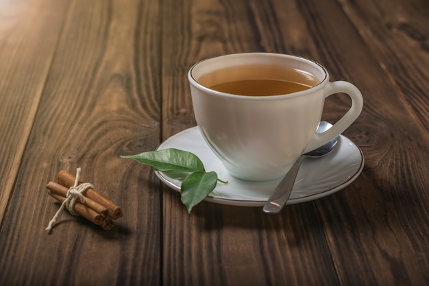 Eine Tasse Tee mit Zimt und grünen Blättern auf einem Holztisch. Ein belebendes Getränk, das für die Gesundheit nützlich ist.