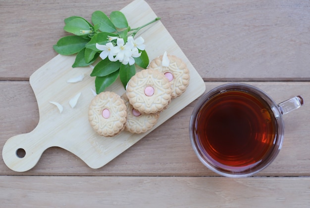 Eine Tasse Tee und Kekse auf dem hölzernen Behälter mit weißen Blumen