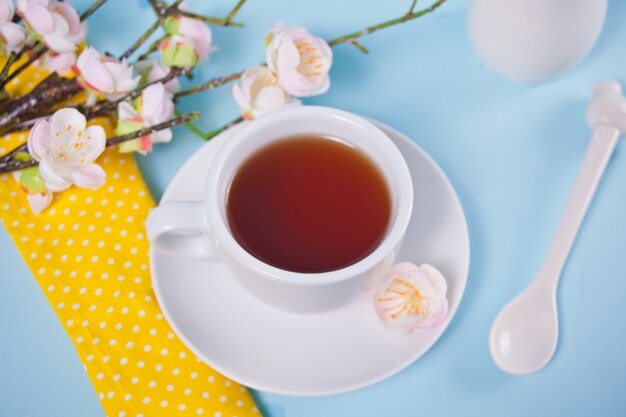 Eine Tasse Tee und Kirsche blüht mit Blumen Sakura auf der blauen Oberfläche. Frühlingskonzept.