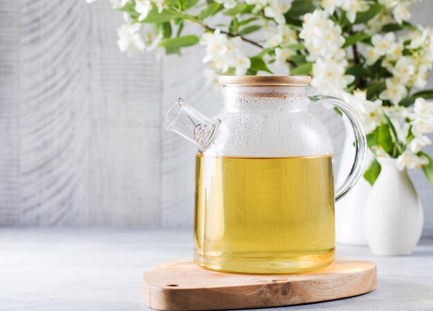 Eine Teekanne mit grünem Tee auf dem Hintergrund eines Zweiges mit Jasminblüten Chinesischer Tee Kopieren Sie Platz