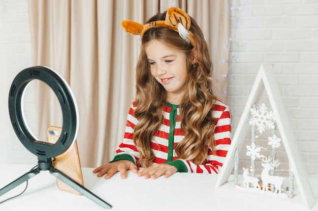 Eine Teenagerin, die über Weihnachten bloggt. Kinderblogger im gestreiften Pyjama nimmt Videos am Telefon auf.