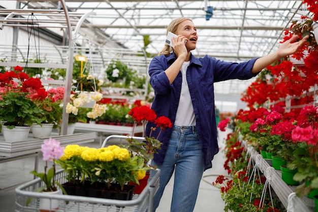 Eine telefonierende Frau mit Karre blickt verwundert auf die Blumen im Gewächshaus
