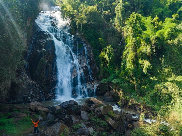 Eine thailändische Landschaftsaufnahme eines stolzen tapferen Mannes, der mit erhobenen Armen vor der Wasserwand steht o