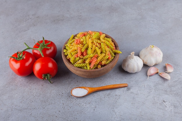 Eine Tonschale mit mehrfarbigen rohen Spiralnudeln mit Knoblauch und frischen roten Tomaten.