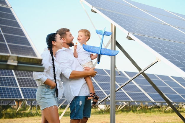 Eine Totalaufnahme einer glücklichen Familie, die zusammensteht und in die Kamera lächelt, mit einem großen Solarpanel im Hintergrund