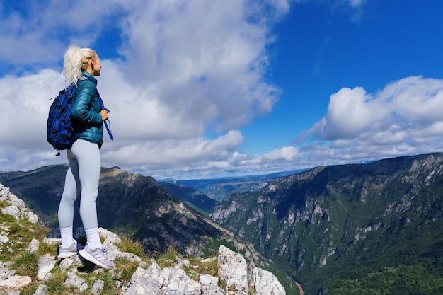 Eine Touristin genießt nach einer Wanderung auf den Berg eine schöne Aussicht auf die Berge