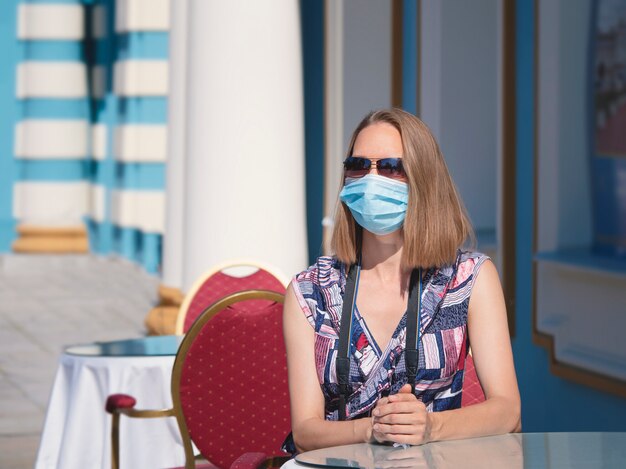 Foto eine touristin in einer medizinischen maske sitzt an einem kaffeetisch auf der straße. sicherheit an einem öffentlichen ort während der epidemie von covid-19.