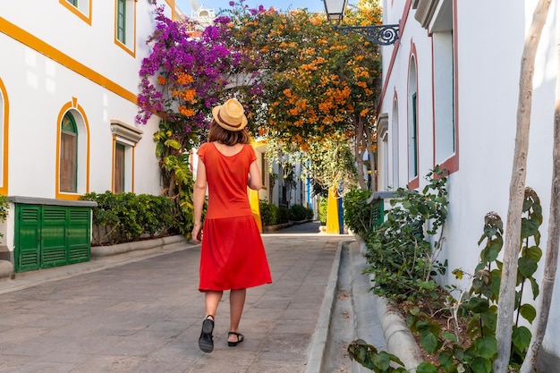 Eine Touristin mit einem roten Kleid im Hafen der blumigen Stadt Mogan im Süden von Gran Canaria, Spanien