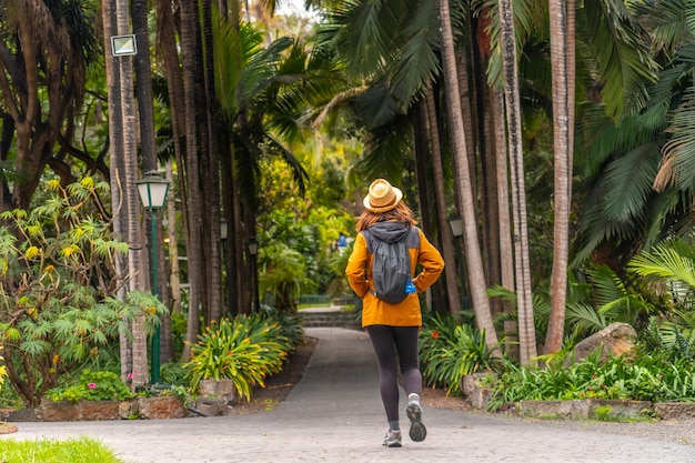 Eine Touristin mit einem Strohhut spazieren in einem tropischen botanischen Garten mit großen Palmen