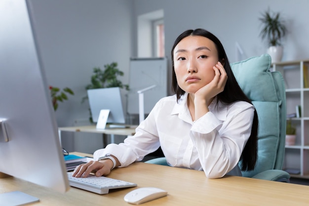 Eine traurige Geschäftsfrau arbeitet in einem modernen Büro, eine Asiatin denkt über die Ergebnisse der Arbeit nach