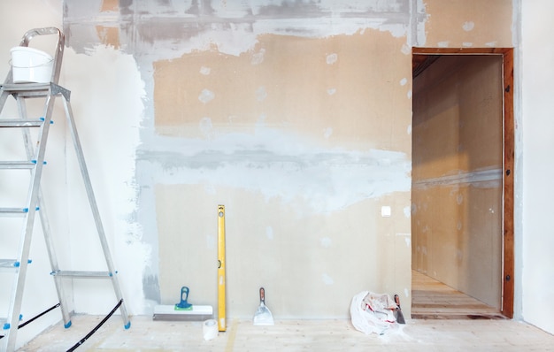 Eine Trittleiter mit Malwerkzeugen in einem Raum in einem Haus oder einer Wohnung. Vorbereitung für Kitt an der Wand oder Malen. Hausreparatur- oder Renovierungskonzept.