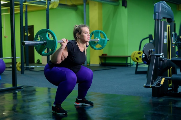 Foto eine übergewichtige frau hockt sich mit einer stange im fitnessstudio ein dickes mädchen macht übungen auf dem gesäß geht in sport, um gewicht zu verlieren