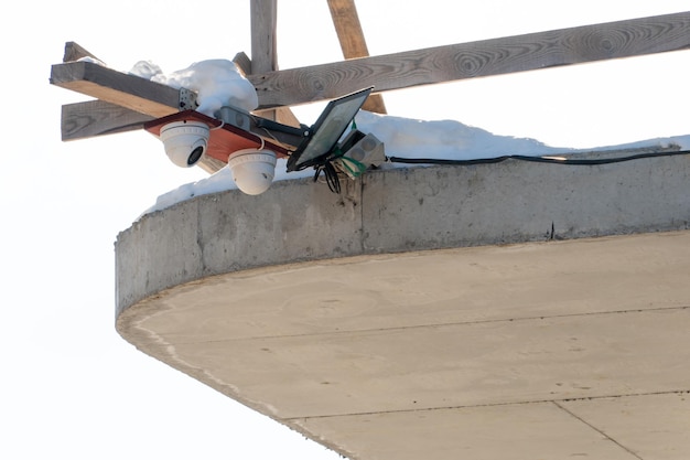 Eine Überwachungskamera, die auf einer hausgemachten Holzhalterung montiert ist, hängt über dem Betonsockel eines im Bau befindlichen Gebäudes, Nahaufnahme Sicherheitssysteme auf der Baustelle