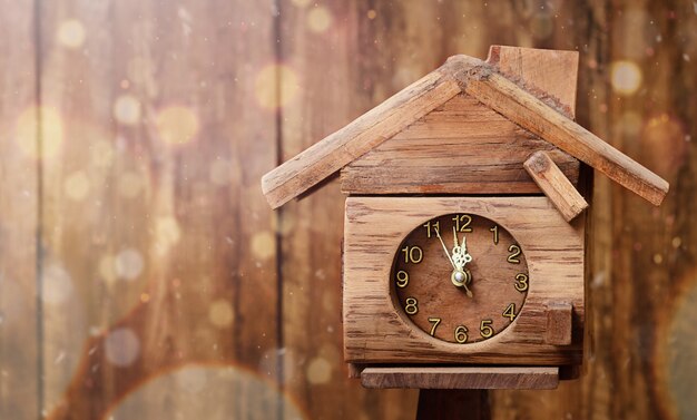 Eine Uhr in Form des Hauses zeigt Mitternacht auf dem Hintergrund der Holzwand