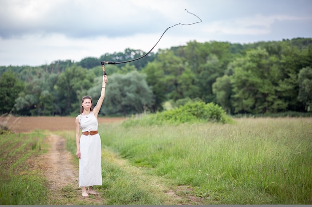 Eine Ungarin steht auf dem Feld in einem Leinenkleid mit einer Peitsche