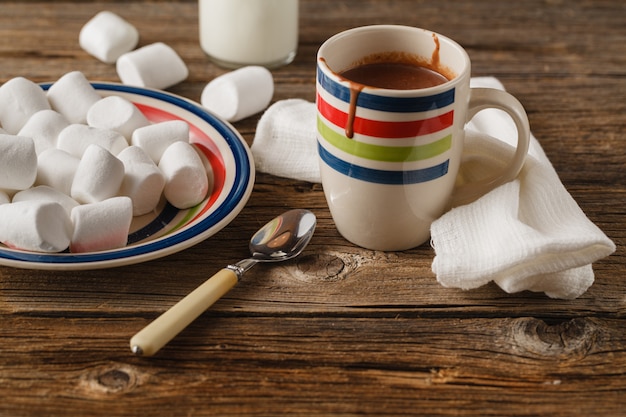 Eine unordentliche Tasse mit heißer Schokolade, Schlagsahne, Marshmallows und Schokoladenkeksen
